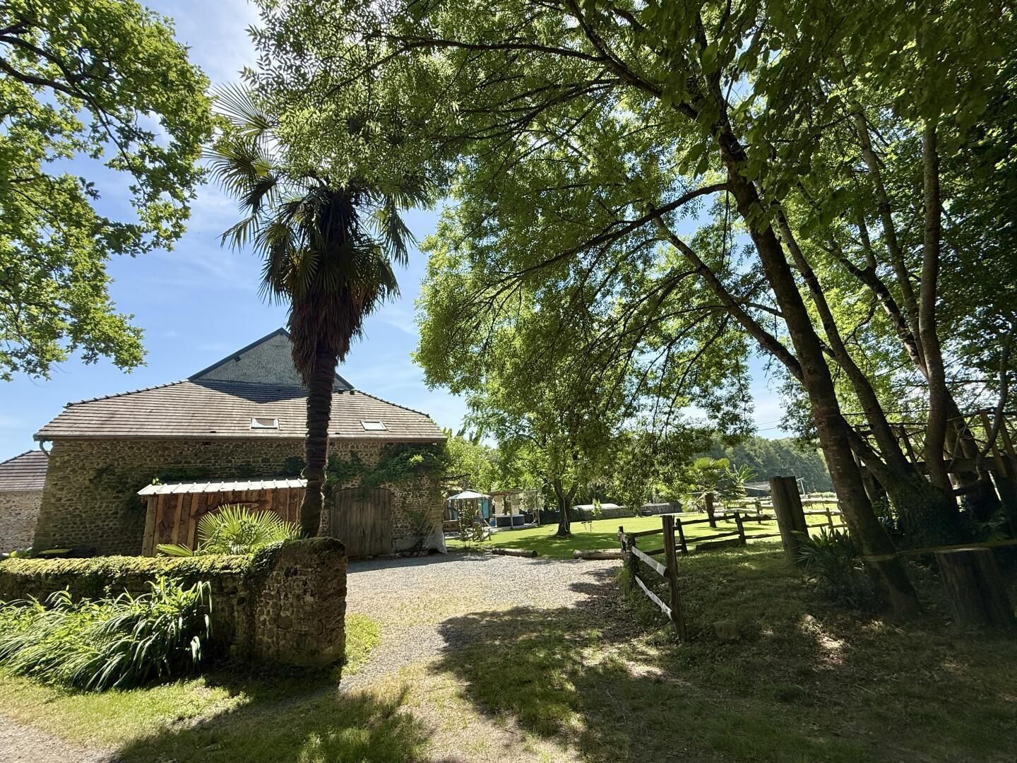 A stone building with a sloped roof, surrounded by a gravel path and lush greenery.