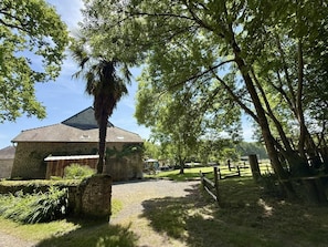 A stone building with a sloped roof, surrounded by a gravel path and lush greenery. - Gite DU Chene - Ledeuix (LEDEUIX)