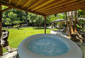 An outdoor hot tub under a wooden pergola with a grassy yard and trees in the background. - Gite DU Chene - Ledeuix (LEDEUIX)