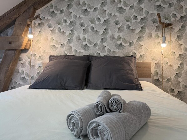 A bed with dark pillows, a white duvet, and rolled towels. - Gite DU Chene - Ledeuix (LEDEUIX)