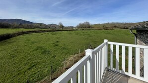 A view from a balcony with a white railing overlooking a green field and distant hills. - Chez Algorry - Aramits (ARAMITS)