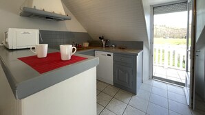 A kitchen with a white countertop, two white mugs, a red placemat, a microwave, and a view of the outdoors through a door. - Chez Algorry - Aramits (ARAMITS)