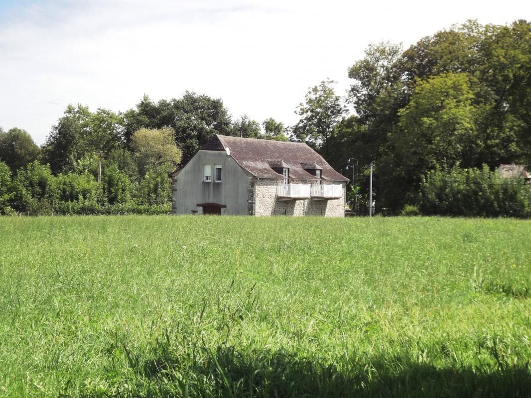 A single-story house with a sloped roof, surrounded by a grassy field and trees.