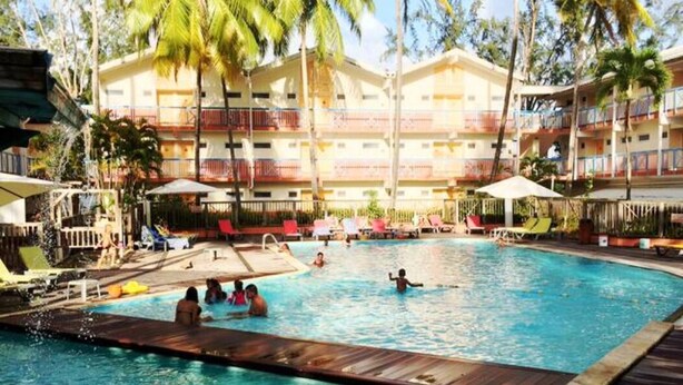 A hotel pool area with multiple swimming pools, lounge chairs, and palm trees. - Charmant T1 avec vue sur la marina (Les Trois-Îlets)