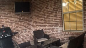 Zona de pati amb parets de maó, un ventilador de sostre, un televisor fixat a la paret i una barbacoa.