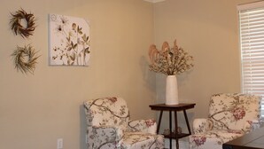 Una habitació amb dues cadires de motius florals, una taula petita amb un ram de flors seques i una il·lustració botànica penjada a la paret.