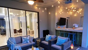 Un patio con mobiliario de mimbre, una mesa de vidrio y luces colgantes.