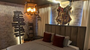 Un dormitorio con pared de piedra, un cartel con nombres como "Hogwarts", una cama con cabecera y un escudo decorativo.