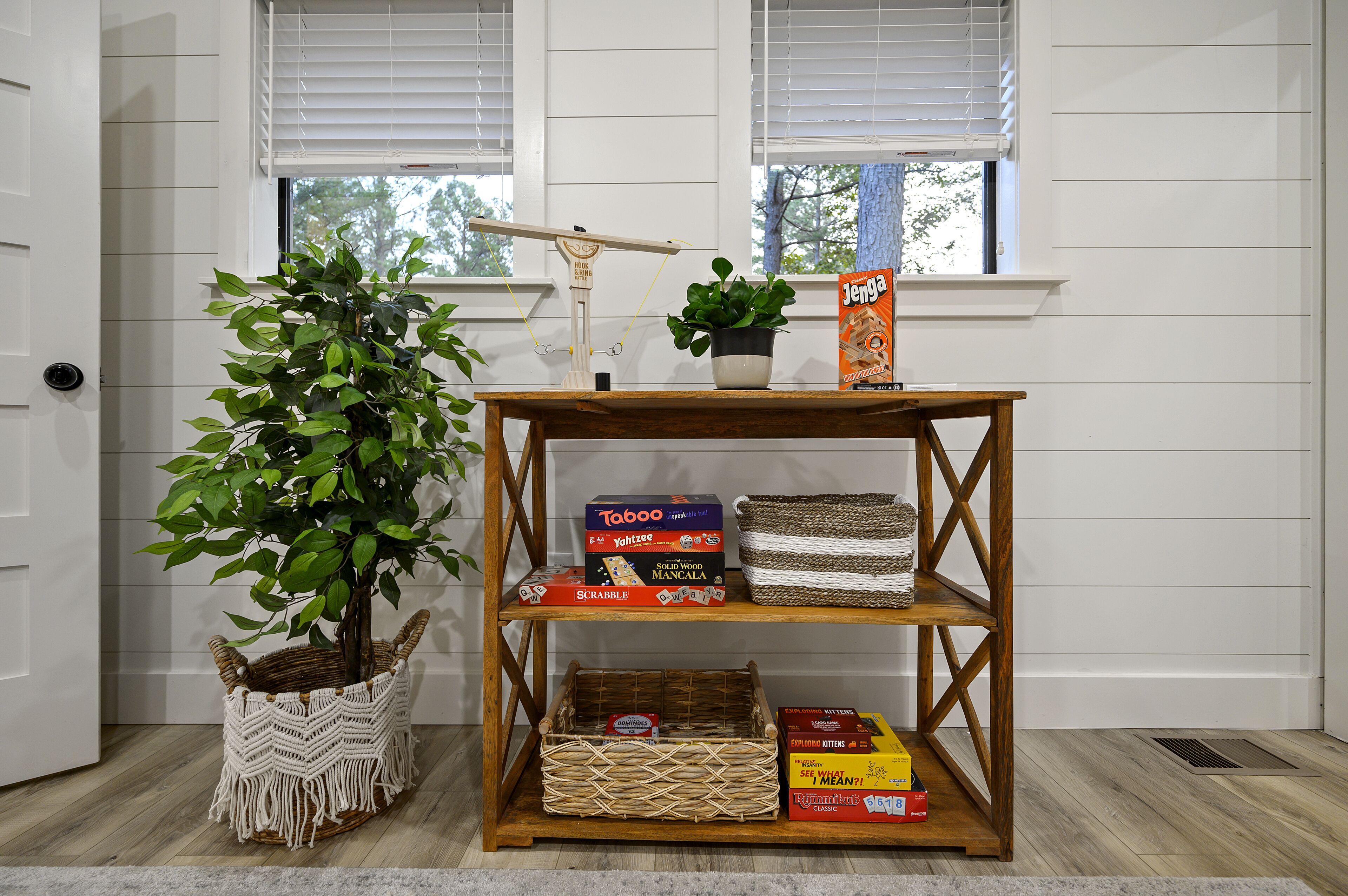 A wooden shelf with board games, a potted plant, and a window with blinds.