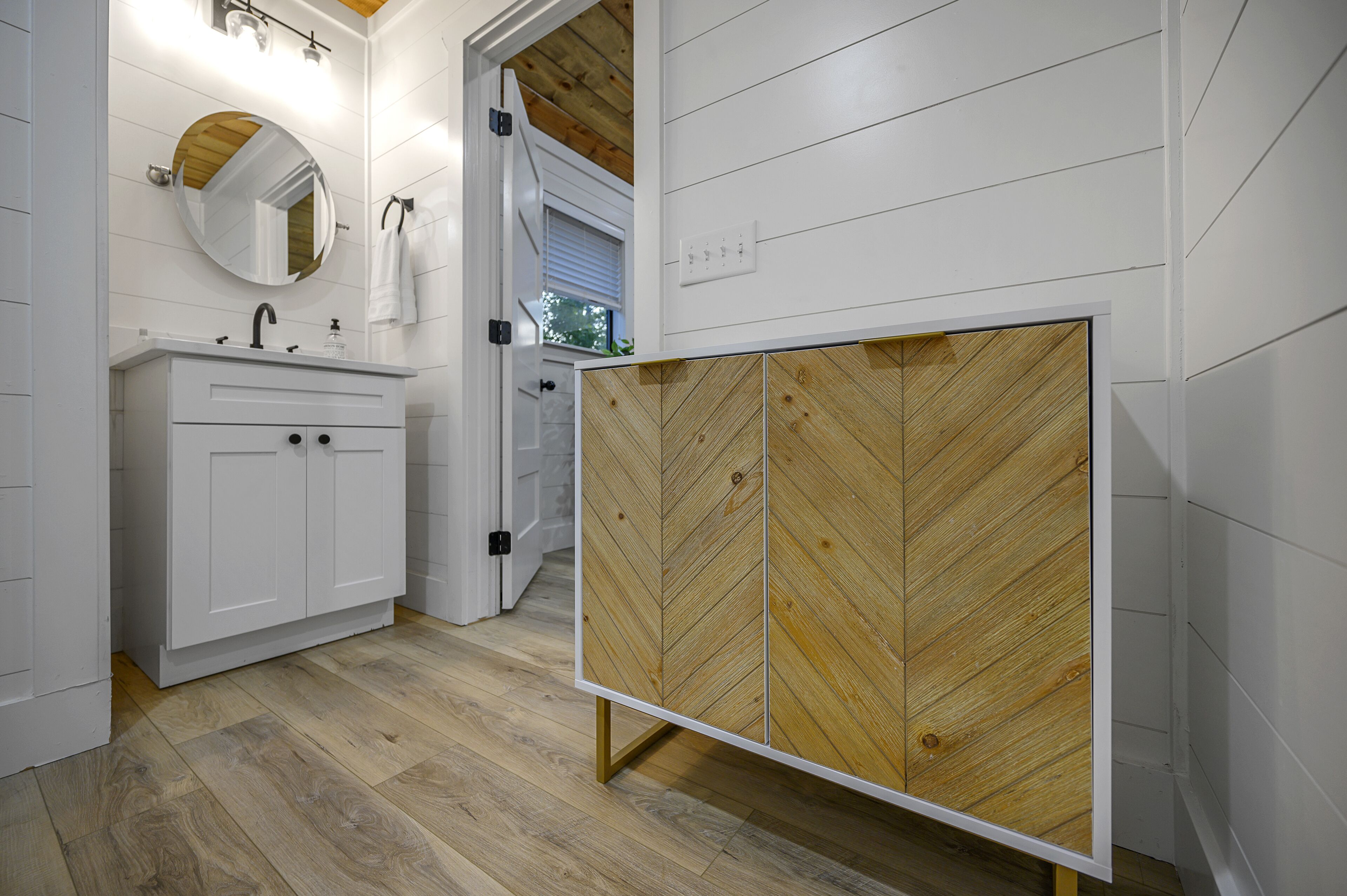 Een moderne badkamer met een houten kastje, een witte wastafel en een spiegel.
