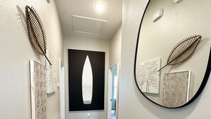 A hallway with wooden flooring, a black and white artwork on the wall, and a round mirror reflecting the artwork. - Gorgeous Beach House w/Pop Up Bar & Community Pool (Rockport)
