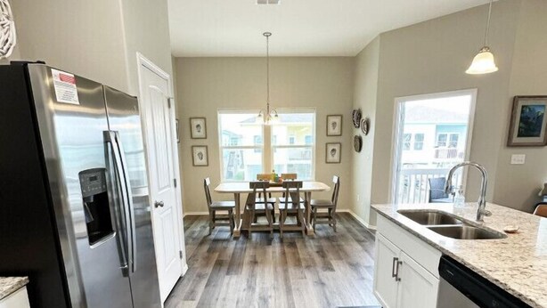 A modern kitchen with a stainless steel refrigerator, wooden dining table, and a large window providing natural light. - Gorgeous Beach House w/Pop Up Bar & Community Pool (Rockport)