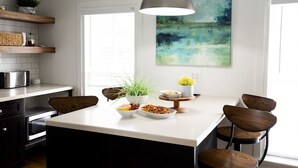 A modern kitchen with a central island, wooden chairs, a pendant light, and a painting on the wall. - Parsonage Suite - Millpond Inn (Clarkston)