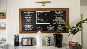 A kitchen with a chalkboard menu listing groceries, beverages, and breakfast options. - The 1842 Suite - Millpond Inn (Clarkston)