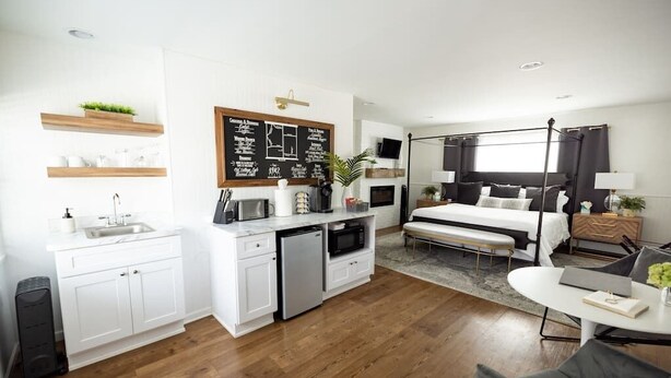 A modern hotel room with a kitchenette, a large bed, a seating area, and a TV. - The 1842 Suite - Millpond Inn (Clarkston)