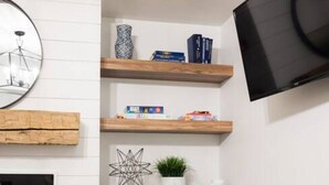 Een moderne woonkamer met witte kasten, een open haard, een flatscreen televisie aan de muur en een gezellige zithoek met een witte poef.