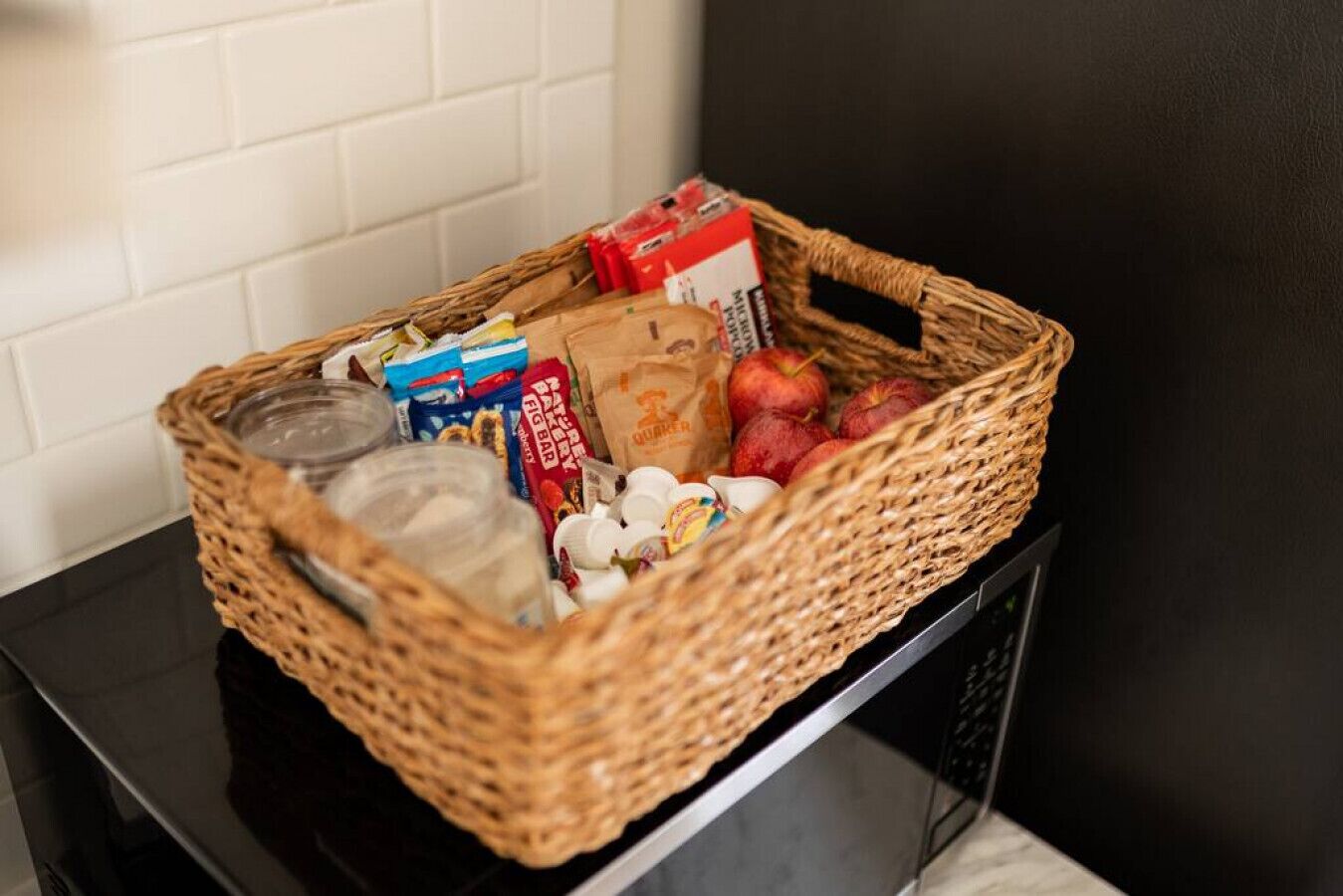 Un panier en osier rempli de divers aliments est posé sur une table noire, devant un mur blanc.