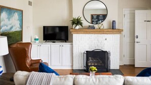 Ein Wohnzimmer mit Kamin aus weißen Ziegelsteinen, einem Fernseher und einem Ledersessel.