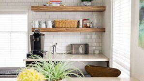 Eine Küche mit weißen U-Bahn-Fliesen, Holzregalen, einer Kaffeemaschine, einem Toaster und einem Blumentopf.