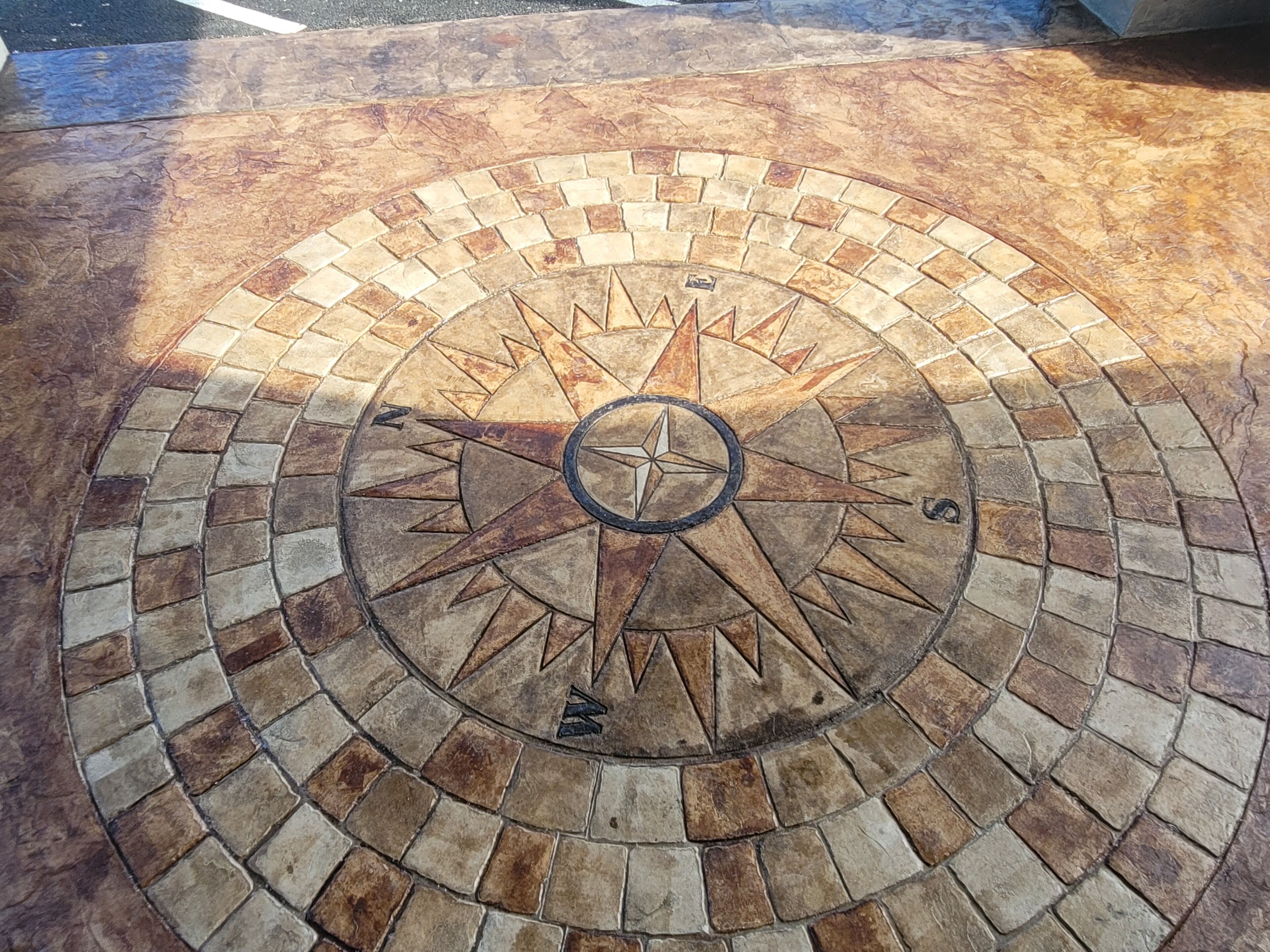 A circular mosaic with a compass design, featuring a central compass rose and radiating patterns.