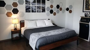 A modern bedroom with a bed, a nightstand, a lamp, and a wall with hexagonal patterns. - The Fireside Inn (Long Beach)