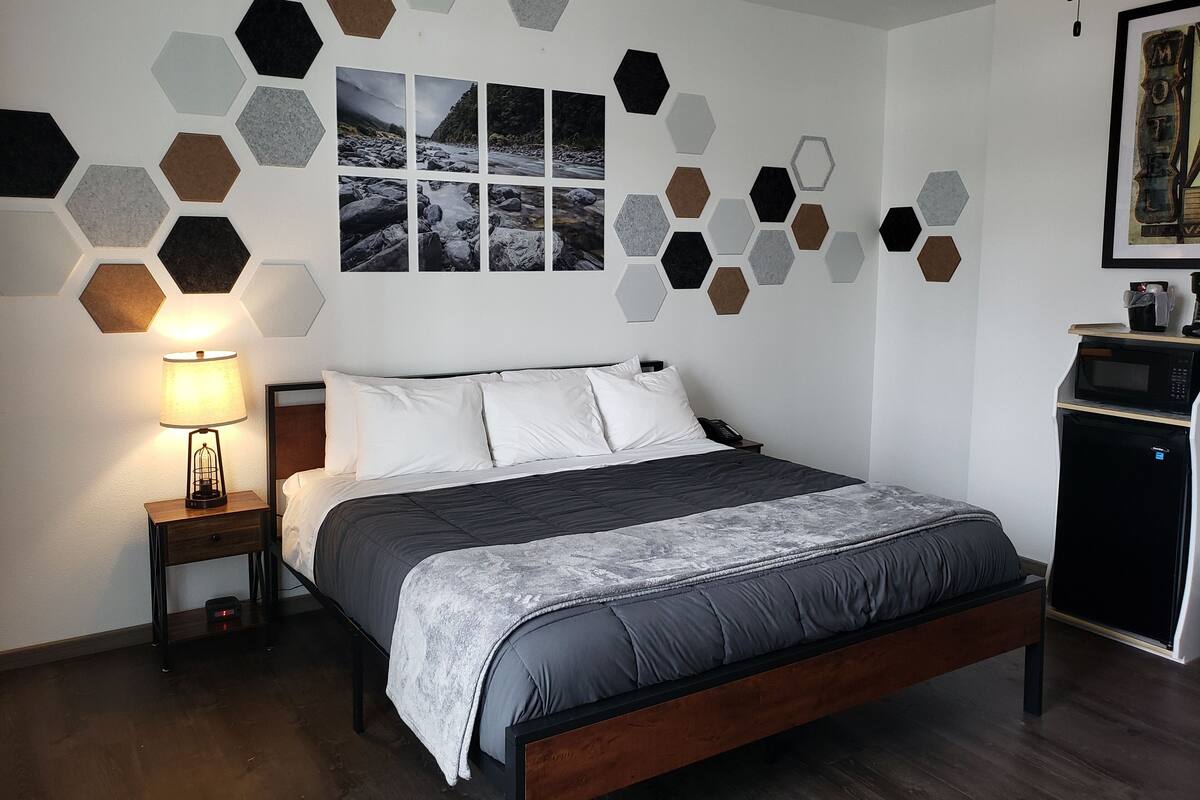 A modern bedroom with a bed, a nightstand, a lamp, and a wall with hexagonal patterns.