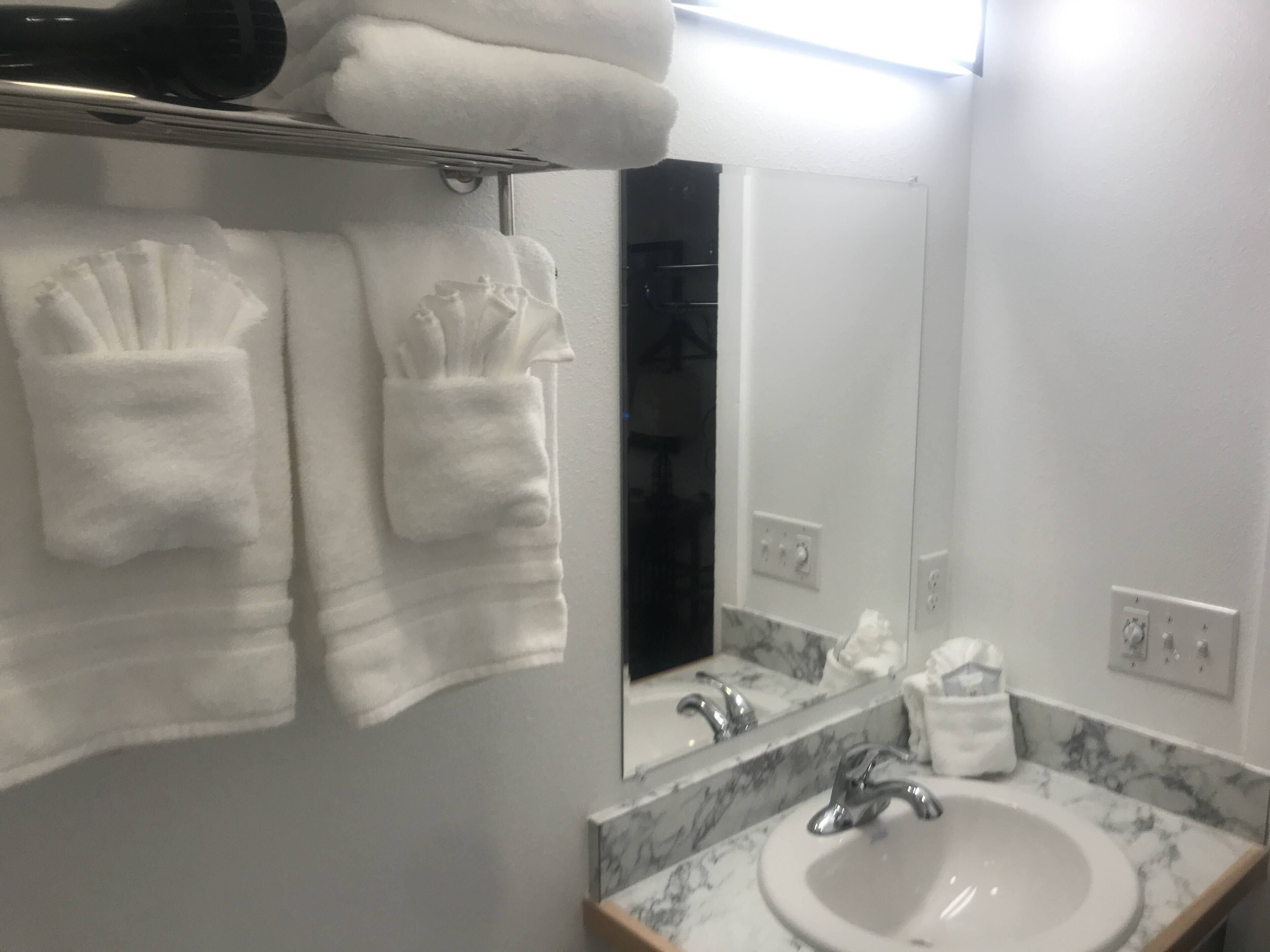A bathroom with a sink, mirror, towel rack, and a bottle of hand soap.