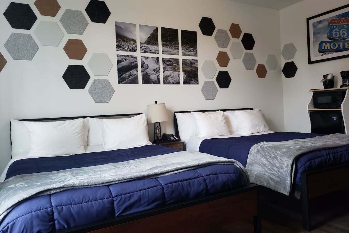 A hotel room with two beds, a wall with hexagonal tiles, a framed picture of Route 66, and a microwave on a shelf.