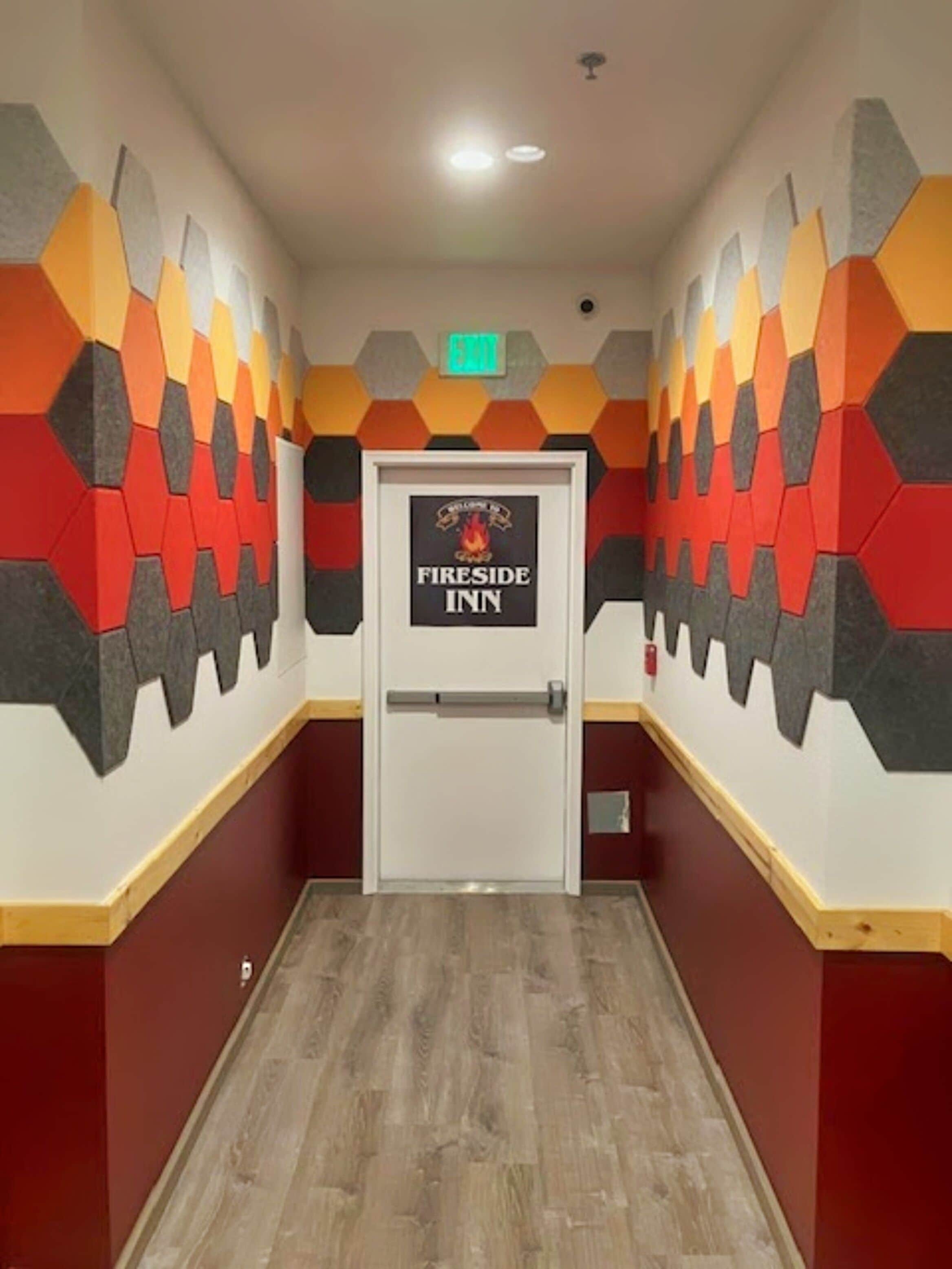 Un pasillo con un papel tapiz de diseño geométrico, una puerta que indica “Fireside Inn” y un suelo de madera.