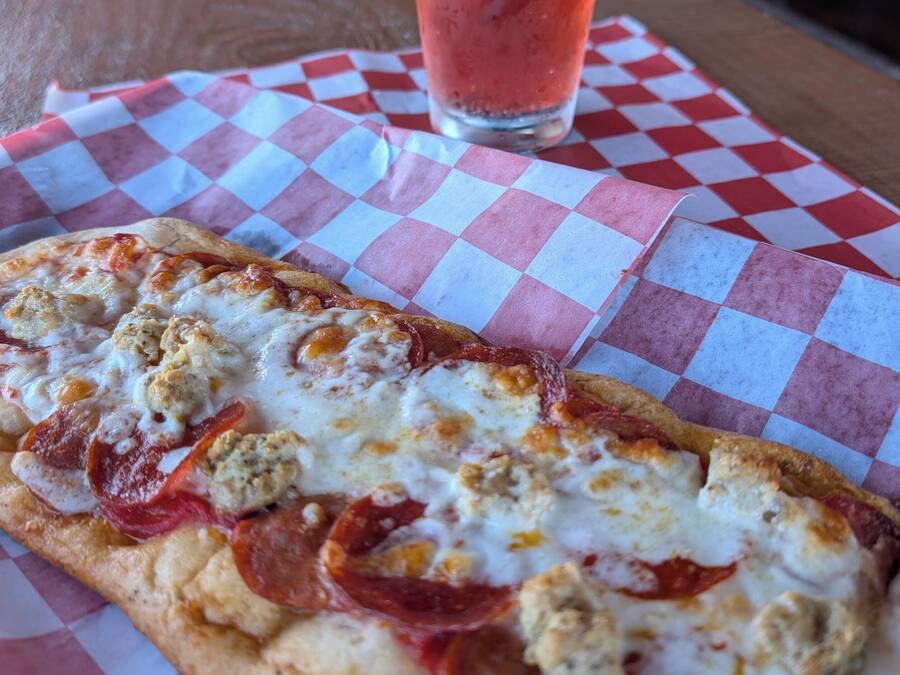 Eine Pizzascheibe mit Peperoni und Wurstbelag auf kariertem Papier.
