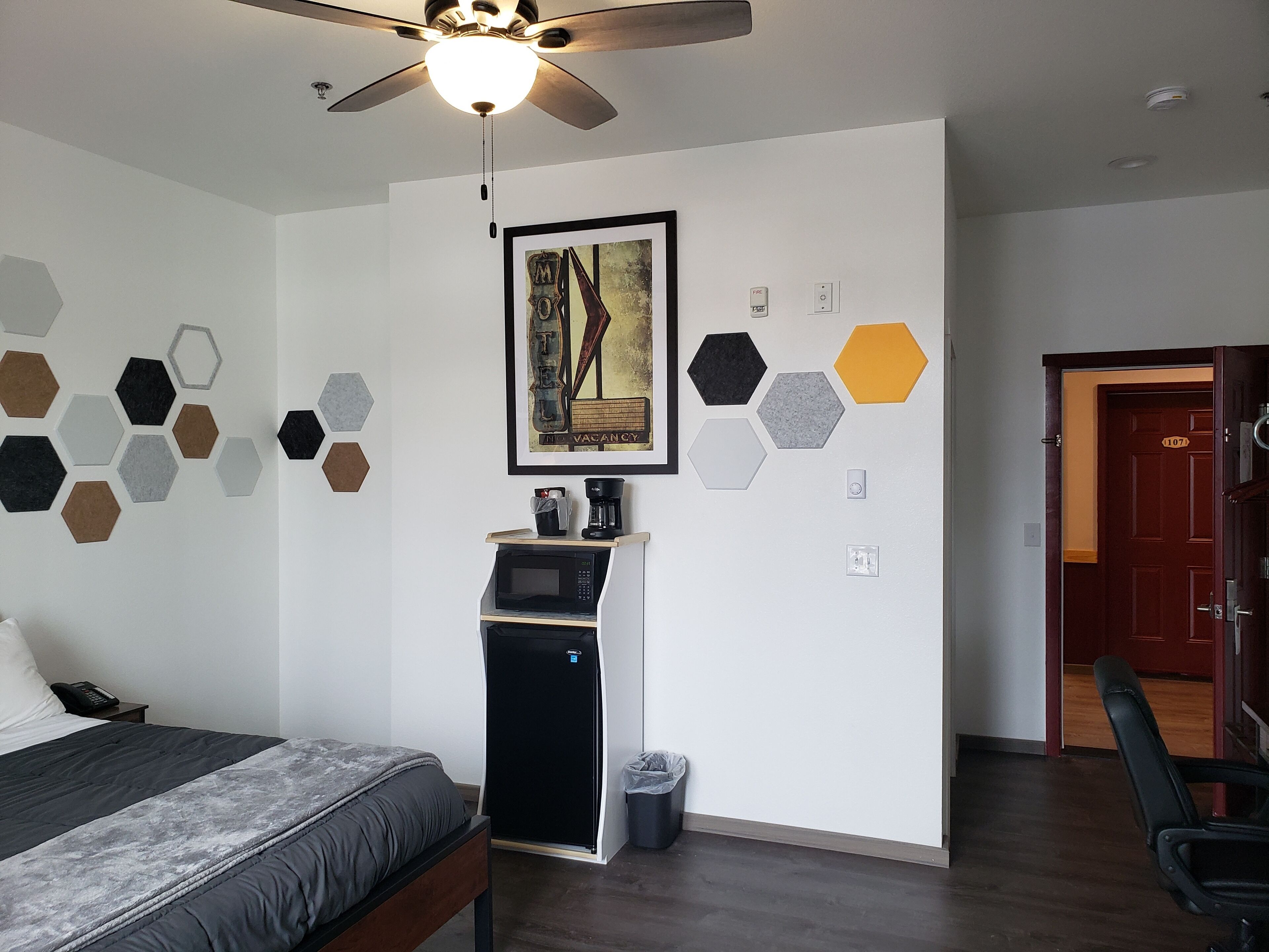 A hotel room with a bed, a ceiling fan, a microwave, a coffee maker, and a trash bin.
