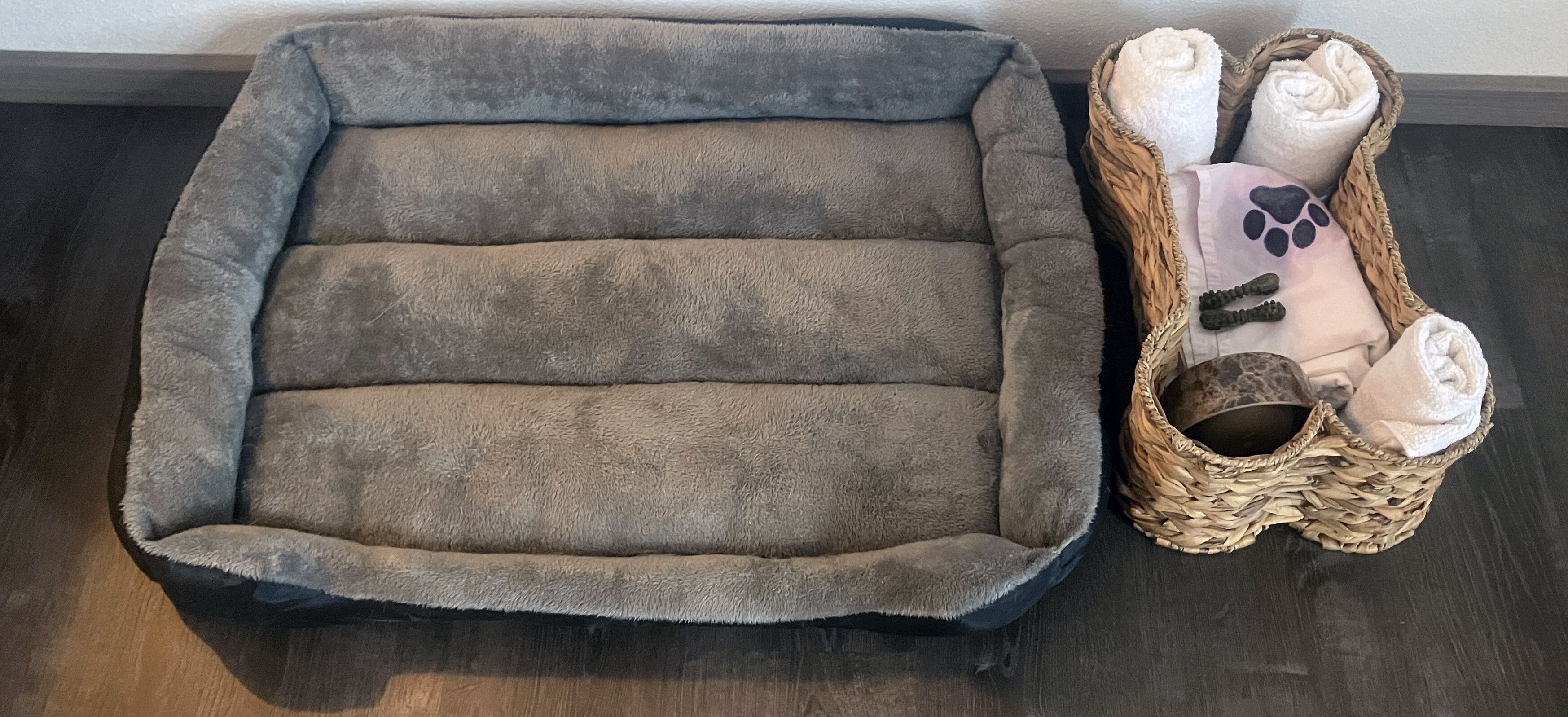 A pet bed with a woven basket containing towels and a paw print pillow.