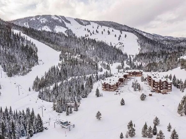 Een bergresort bedekt met sneeuw, met meerdere gebouwen, skiliften en dichte bossen.