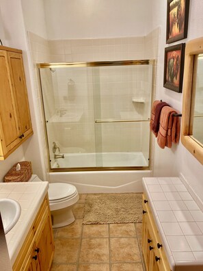 Een badkamer met een douche met glazen wand, een toilet, een wastafel, houten kastjes en een beige vloerkleed.