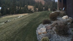 Edifici amb fonamentació de pedra i estructura de fusta, envoltat d'un jardí ben cuidat i un turó forestal.