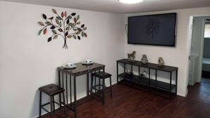 A living room with a dining table, two chairs, a console table with decorative items, a wall-mounted TV, and a ceiling light. - A newly remodeled 1BD&1BR private whole Guest-home to yourself! (Lancaster)