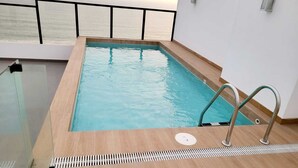 Une piscine rectangulaire intérieure, dotée d’une terrasse en bois et d ’une échelle en métal.