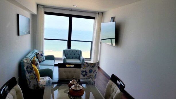 Un salon moderne avec un canapé, des fauteuils, une table basse en verre et une vue sur la plage.