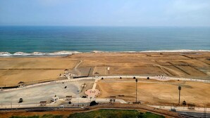 Vue aérienne d’une zone côtière comprenant un vaste espace ouvert, un parking et une promenade le long de la plage.