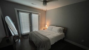Ein Schlafzimmer mit einem Bett, einem Nachttisch, einer Lampe und einem Fenster mit Jalousien.