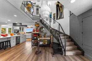 A modern kitchen with a central island, a staircase with a metal railing, and various decorative items on the walls.