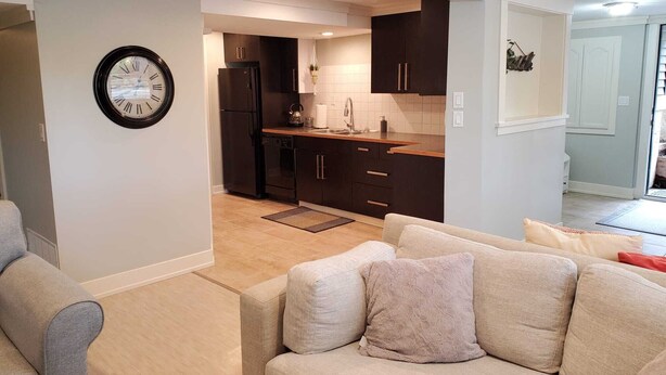 Un salon moderne avec un canapé beige et un coin cuisine doté de meubles sombres et d’un réfrigérateur noir.