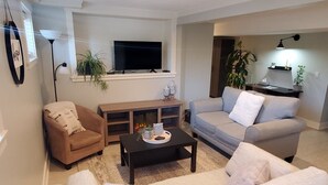 Un salon avec un fauteuil marron, un canapé gris, une table basse noire et un téléviseur fixé au mur.