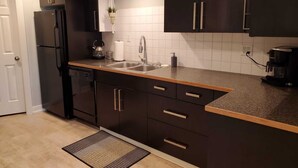 Une cuisine moderne avec des meubles de couleur sombre, un réfrigérateur en acier inoxydable, un évier et une machine à café.