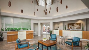 Un hall d’entrée spacieux avec un comptoir de réception, des fauteuils en cuir bleu, une table basse en bois et des lampes suspendues.