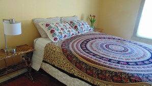 Una cama con una colcha estampada, una lámpara de noche y un jarrón con flores.