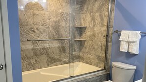 A bathroom with a glass-enclosed shower, a bathtub, a toilet, and a sink. - The Spacious Canal Condo (Caseville)