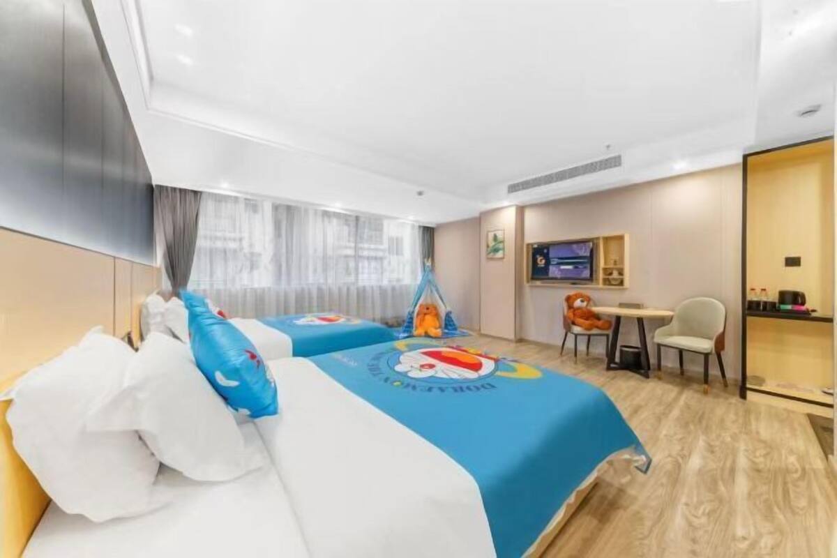 Ein Hotelzimmer mit zwei Betten, einem Schreibtisch, einem Sessel, einem Fernseher und einem Fenster mit Vorhängen.