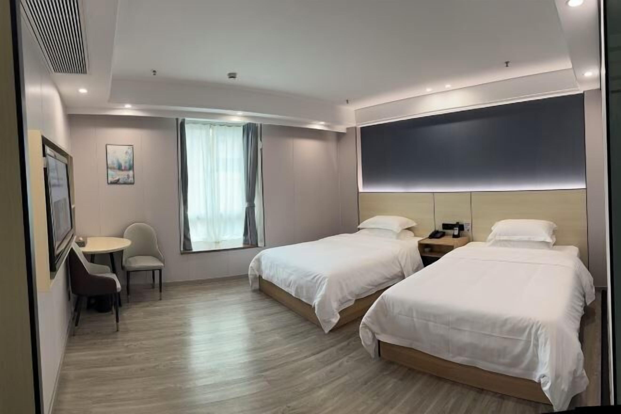 A hotel room with two single beds, a desk with a chair, a window with curtains, and a painting on the wall.