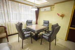 A dining area with a rectangular table and four chairs, a ceiling light, and an air conditioning unit on the wall.